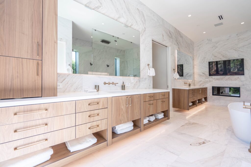 modern bathroom with double vanities, large mirrors, wood cabinetry, marble walls and floors—perfect for your next bathroom renovation. open shelves with towels and a freestanding bathtub complete this stunning bathroom makeover.
