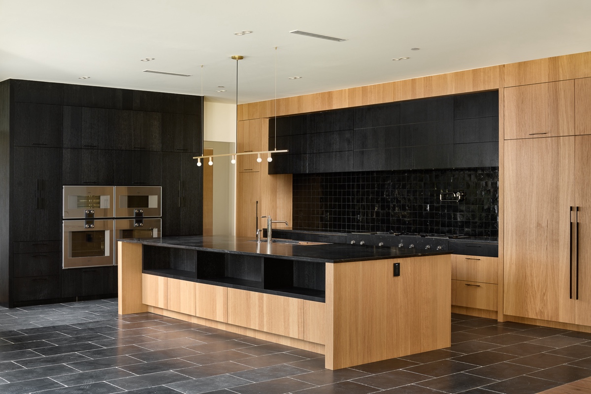 Modern kitchen remodel with light wood cabinetry, black countertops, a central island with sink, built-in appliances, and a black tile backsplash on a dark tiled floor—perfect for your next kitchen renovation.