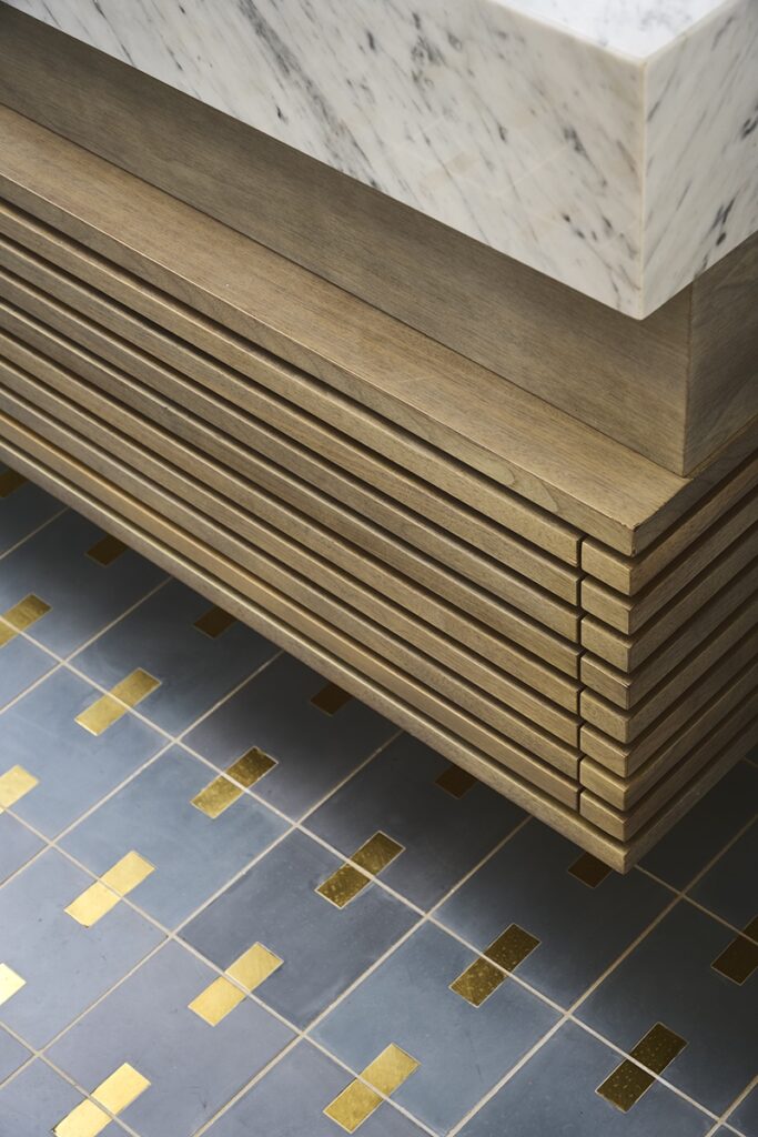 Close-up of a marble countertop with a wooden slatted base above a blue tiled floor featuring a gold square pattern—an inspiring detail for your next bathroom makeover.