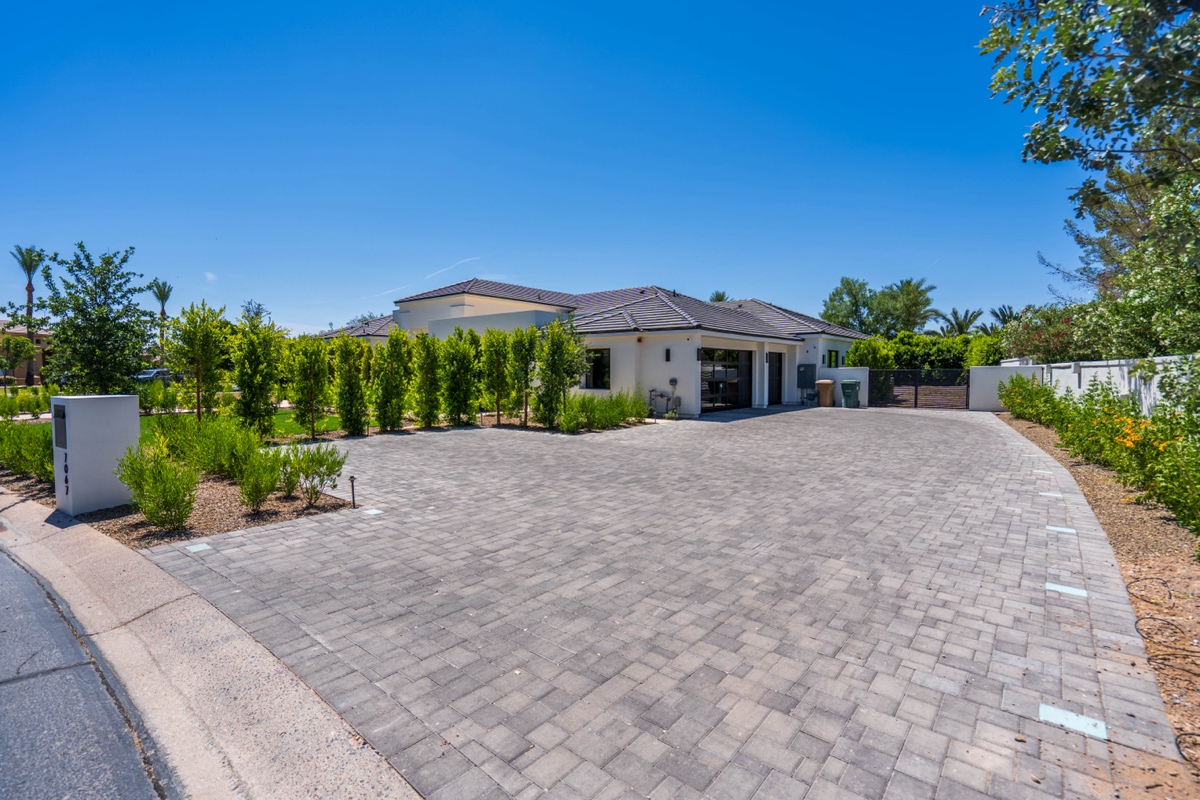 A modern single-story house with a large paved driveway, surrounded by greenery and a clear blue sky overhead—perfect for embracing outdoor living.