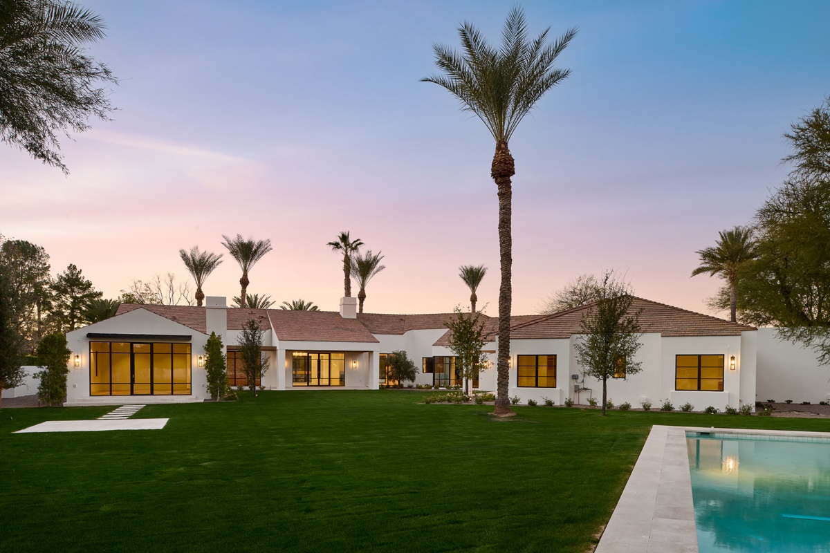 Modern single-story white house with large windows, surrounded by palm trees, a spacious lawn, and a swimming pool at sunset—perfect for embracing outdoor living.