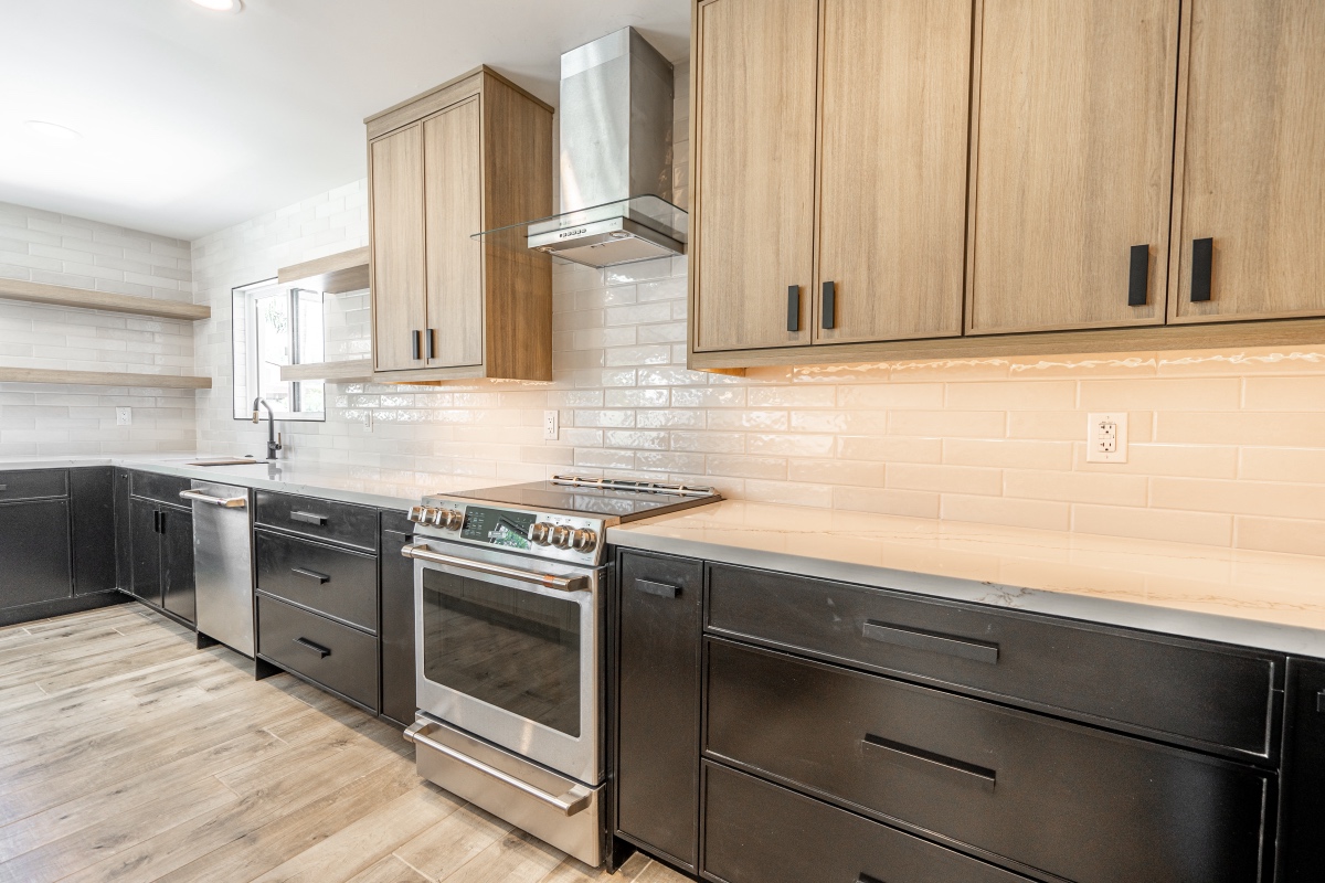 modern kitchen remodeling with black lower cabinets, light wood uppers, stainless steel appliances, a tile backsplash, and wood look flooring.