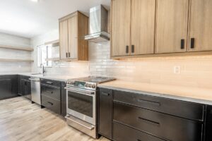 Modern kitchen remodeling with black lower cabinets, light wood uppers, stainless steel appliances, a tile backsplash, and wood-look flooring.