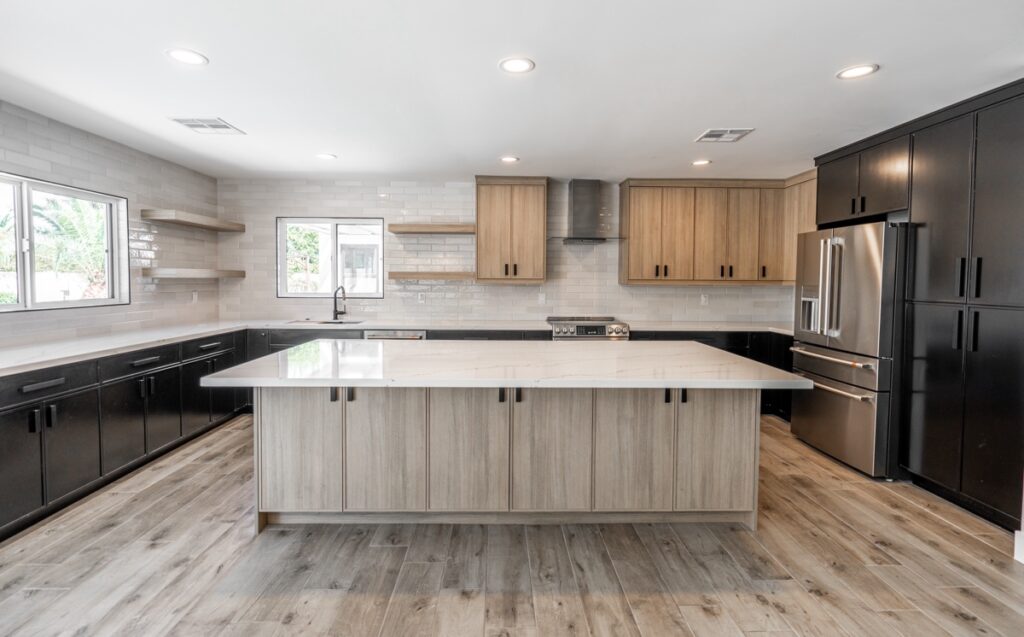 Modern kitchen remodeling with a large island, wood and black cabinets, stainless steel appliances, tile backsplash, floating shelves, and wood-look flooring.