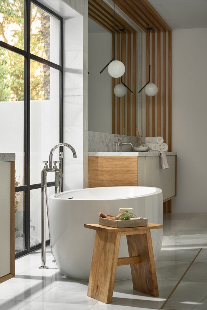 Modern bathroom renovations feature a freestanding white bathtub, wooden stool, floor-to-ceiling window, and minimalist vanity with round pendant lights and wooden accents.