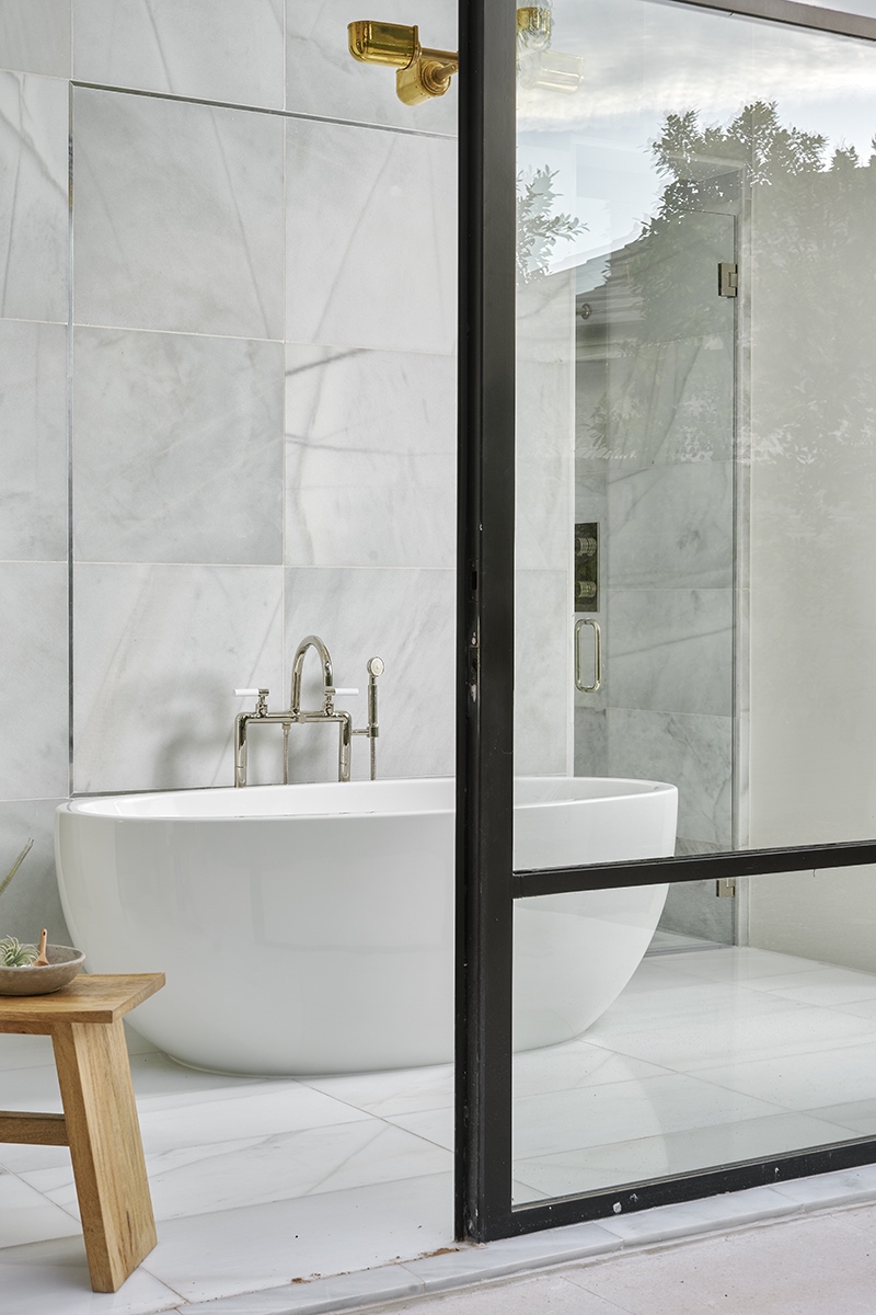 Modern bathroom with a white freestanding bathtub, marble walls and floors, a wooden stool, and a glass shower enclosure—perfect inspiration for your next bathroom remodeling or makeover project.