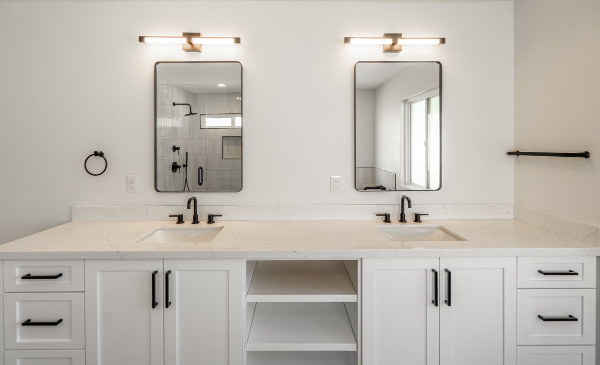modern bathroom with double sinks, white cabinets, black fixtures, two rectangular mirrors, and wall mounted lights above each mirror.