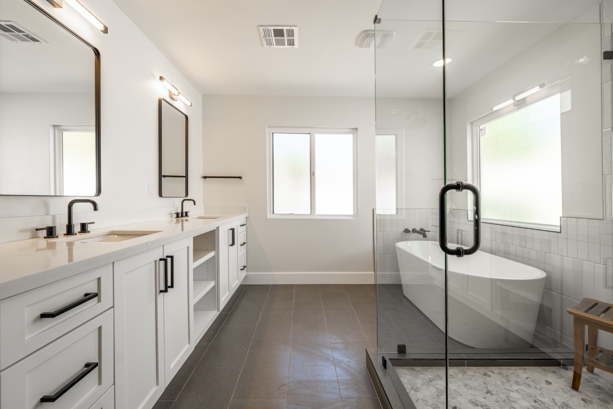 modern bathroom with white double sink vanity, black fixtures, large glass enclosed shower, freestanding bathtub, and gray tile floor.