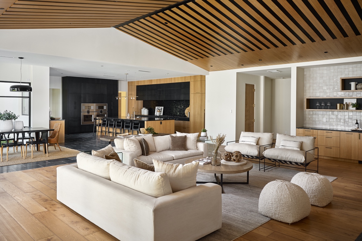 modern open concept living space with neutral sofas, wood flooring, slatted wood ceiling, kitchen with black cabinets, and dining area with a black table and chairs.
