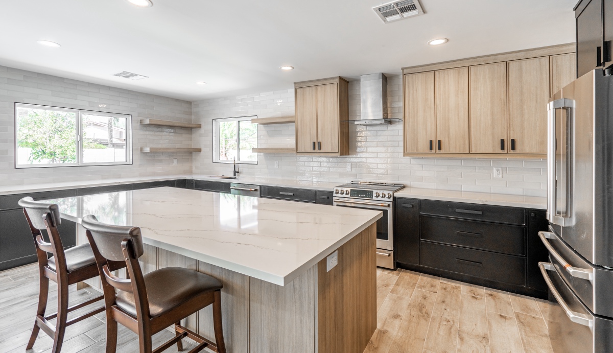 modern kitchen with light wood cabinets, white marble island, stainless steel appliances, tile backsplash, and two wooden chairs. large windows provide natural light.