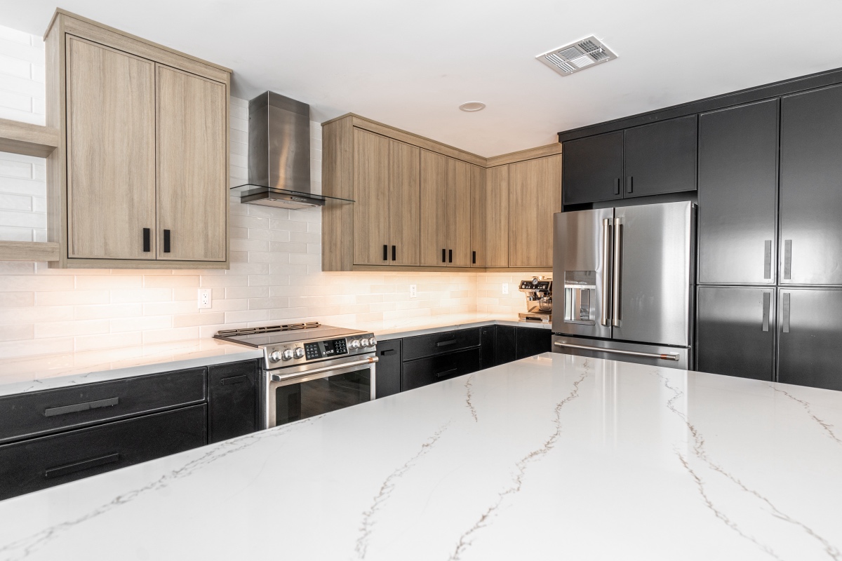 modern kitchen with light wood and black cabinets, stainless steel appliances, white subway tile backsplash, and a large white marble countertop island.