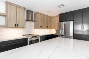 Modern kitchen with light wood and black cabinets, stainless steel appliances, white subway tile backsplash, and a large white marble countertop island.