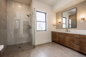 Modern bathroom with a glass-enclosed shower, a large window, dual-sink wooden vanity, rectangular mirror, and wall-mounted lights.