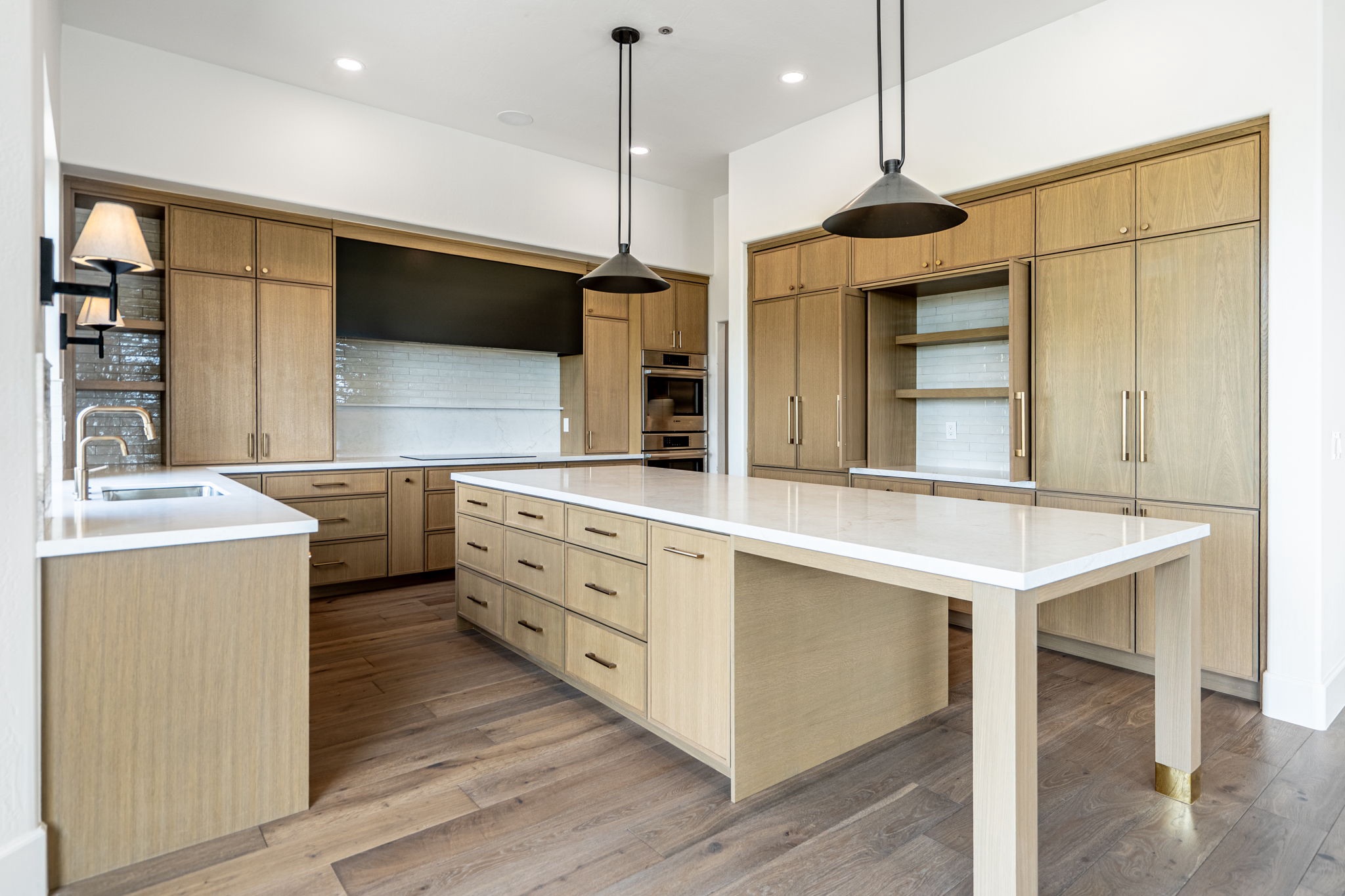 Modern kitchen with light wood cabinets, a large island with white countertops, built-in appliances, pendant lights, and hardwood floors.