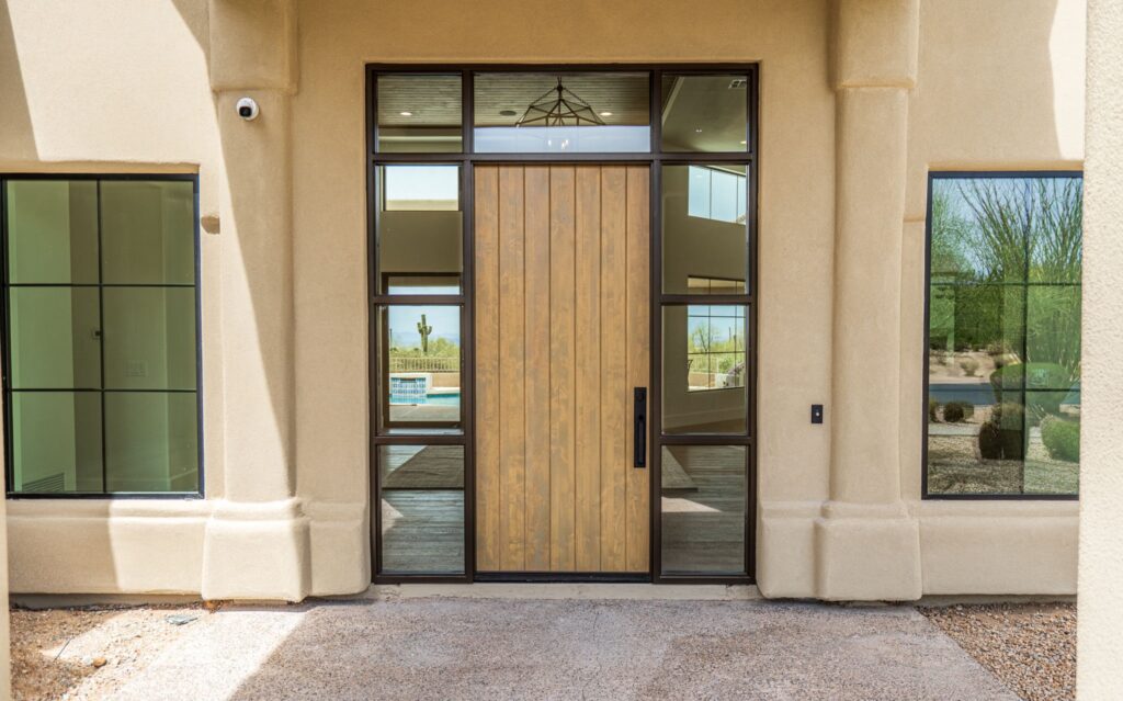 modern front door with vertical wood panels and glass side panels, surrounded by beige stucco exterior and large windows.