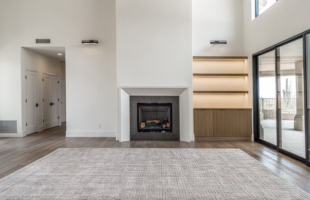 A modern living room with a fireplace, built-in shelves, large rug, wood flooring, double doors, and sliding glass doors to a balcony.