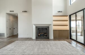 A modern living room with a fireplace, built-in shelves, large rug, wood flooring, double doors, and sliding glass doors to a balcony.