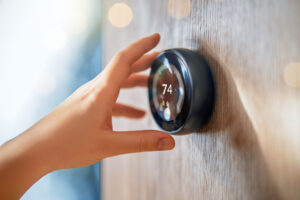 A hand adjusts a round smart thermostat mounted on a wooden wall, displaying 74 degrees—an easy step toward better home efficiency.