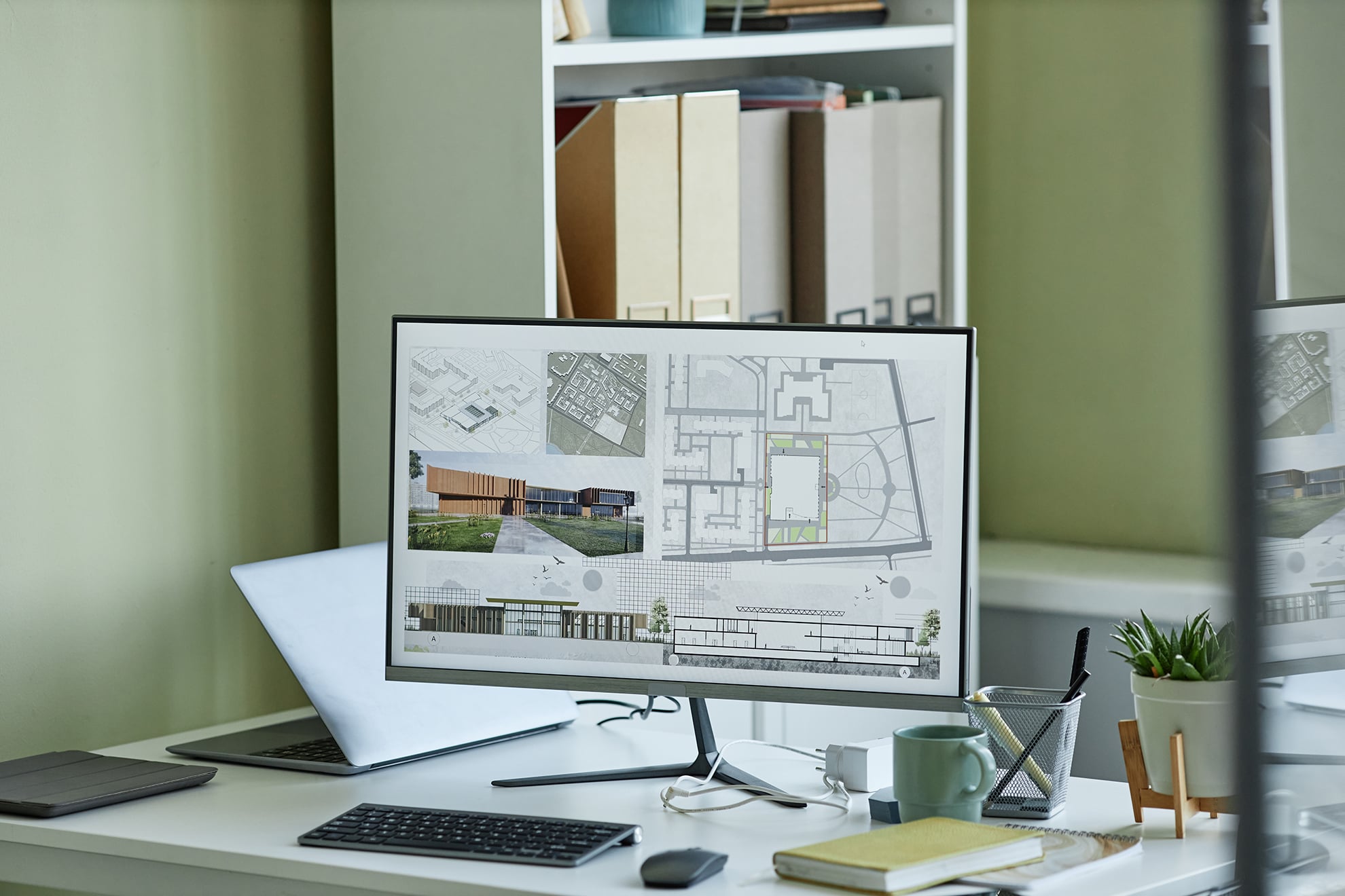 A computer monitor displays architectural plans, blueprints, and building renderings on a desk with a laptop, plant, stationery, and shelves in the background—perfect for showcasing professional Blueprint Design Services.